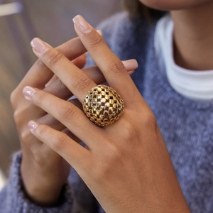 Bague dorée imposante à texture pointillée sur main de mannequin et fond en tricot bleu