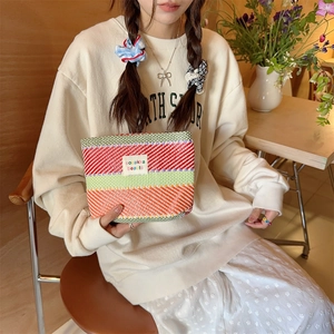 Model holding a colorful striped woven makeup bag in a cozy indoor setting