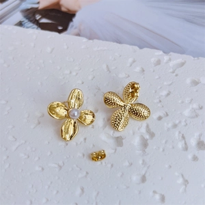 Close-up of golden petal earrings with irregular texture and center faux pearl inlay
