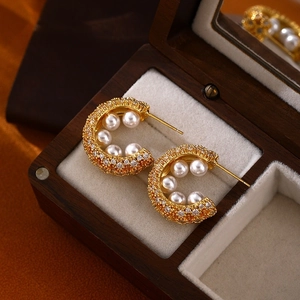 Detail of vintage C-shaped gold earrings with zircons and pearls in a wooden jewelry box