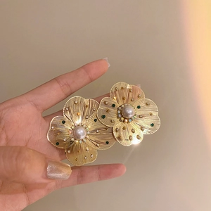 Macro detail of golden hollow flower earring with centered pearl and colorful rhinestones