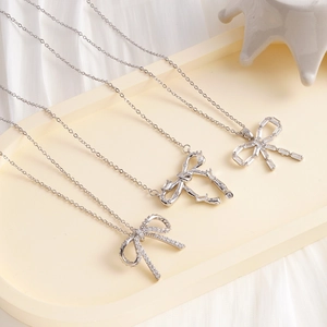Three elegant silver bow necklaces with zircon stones on a beige tray with soft lighting