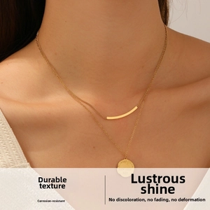 Close-up of gold double-layer necklace with engraved round tag and curved bar pendant
