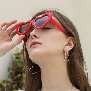 Chic red heart shaped sunglasses with matching silver earrings on a fashion model