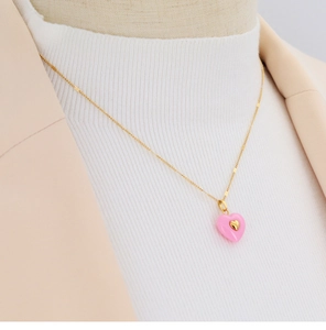 Close-up of elegant gold necklace with pink heart pendant on model in white knitwear
