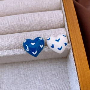 Detail of heart-shaped blue and white enamel earrings with V-pattern in a jewelry box