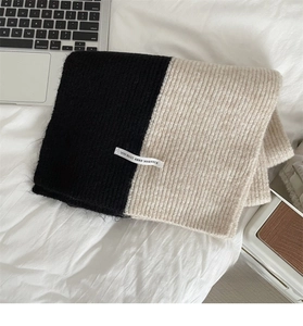 Close-up of color-block knit scarf featuring ribbed texture and a minimalist slogan tag
