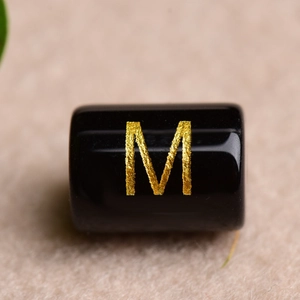 Macro shot of black agate bead with gold letter M engraving for DIY jewelry