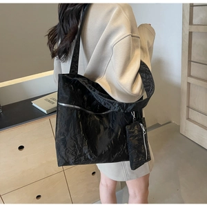 Detail of black glossy wrinkled tote bag featuring side metal zipper and matching small pouch