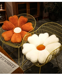 Detail of flower-shaped plush pillows in caramel and off-white on gold iron chairs