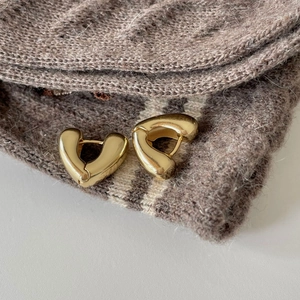 Macro shot of minimalist gold heart-shaped chunky hoop earrings on brown knit fabric