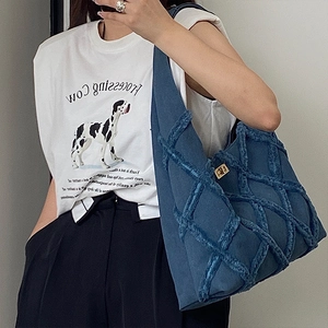 Detail of blue denim shoulder bag with diamond woven raw edges and golden twist lock