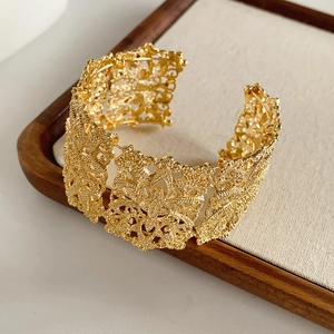 Macro detail of golden retro hollow floral pattern cuff bracelet with matte texture