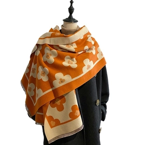Orange floral print winter shawl with tassels on a black coat mannequin display