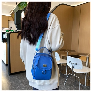 Detail of blue nylon crossbody bag featuring a front flap and metallic ring accent