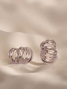 Macro detail of rose gold C-shaped earrings with layered spiral winding on sand background