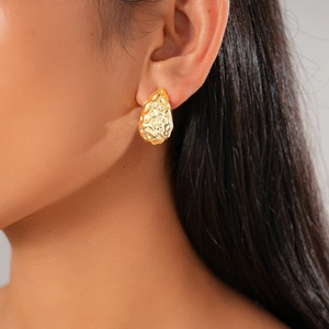 Close-up of gold teardrop earrings with hammered texture on female model's ear