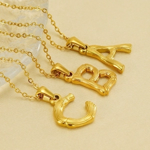 Gold stainless steel initial necklaces with bamboo texture on gold fabric background