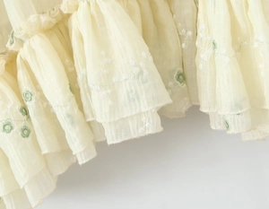 Dettaglio macro della gonna in chiffon beige con volant a strati e ricami floreali