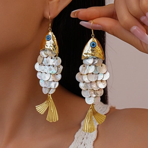 Golden fish shaped earrings with white shell disks worn by a model in a close-up view
