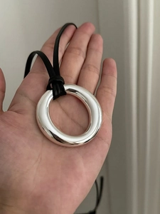 Close-up of a large polished silver ring pendant with black cord held by a hand