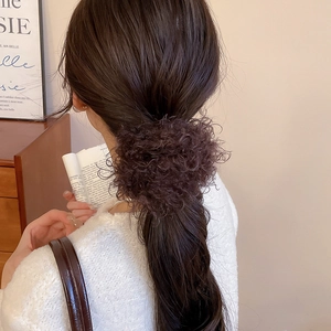 Detail of a dark brown plush curly hair tie styled on a woman's ponytail in a cozy setting