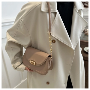 Side view of beige leather crossbody bag with metal buckle and chain strap on model