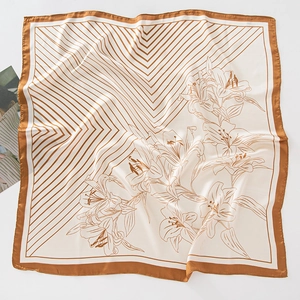 Dettaglio di un foulard in seta con motivi a giglio dorati e strisce su sfondo bianco
