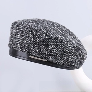 Detail of tweed beret hat featuring black faux leather trim and silver metal label