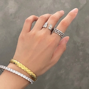 Close-up of layered zircon rings and gold textured cuff bracelet set on a grey background