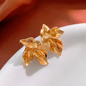Boucles d'oreilles dorées en forme de feuilles avec finition miroir sur assiette blanche