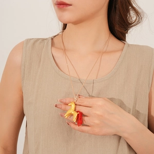Detail of a golden horse pendant with a vibrant red tassel on a long cord necklace