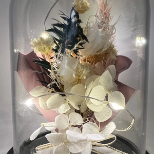 Close-up of preserved flower arrangement in cylindrical dome with LED lights and gold ribbon