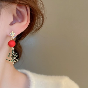 Detail of Christmas earrings featuring a smiling star, red bead, and green rhinestone tree