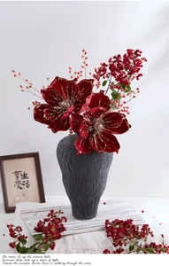 Close-up of artificial red poinsettias and berries in a black textured ceramic vase