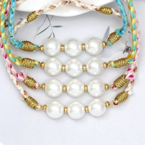 Close-up of colorful woven bracelets with white glass pearls and gold thread detail