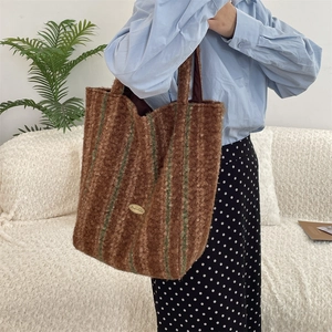 Detail of dark brown faux shearling tote with green stripes and gold logo plate