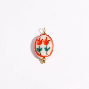 Close-up of white ceramic oval pendant with red tulip patterns and 18K gold-plated parts