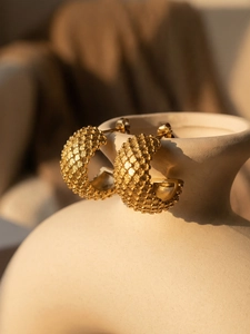 Detail of 18k gold plated C-shape earrings with textured grain finish on ceramic vase