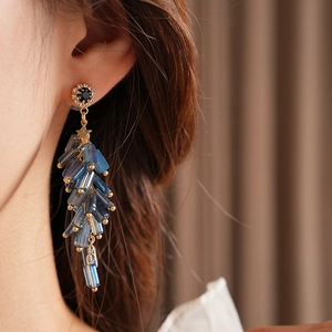 Macro detail of firecracker tassel earrings with blue crystals and gold setting on model