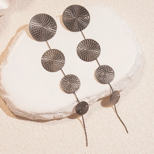 Détail de disques métalliques texturés sur de longues boucles d'oreilles pendantes