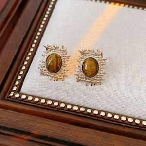 Close-up of vintage gold square earrings with oval tiger eye stone on fabric