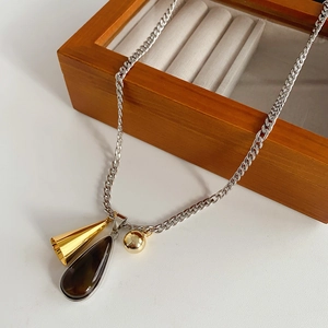 Detail of titanium steel necklace with gold cone and brown teardrop charms on wood box