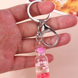 Detail of a clear glass wishing bottle keychain with pink liquid and tiny sea shells
