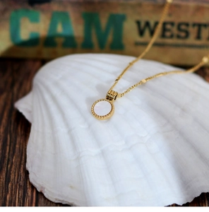 Detail of round white mother-of-pearl pendant on gold-plated chain displayed on a seashell