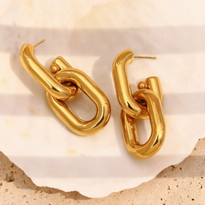 Close-up of gold hollow chain link earrings on a white shell tray with warm lighting