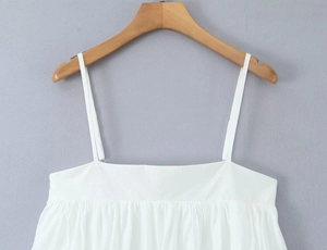 Detail of white spaghetti strap top with subtle pleated texture on wooden hanger