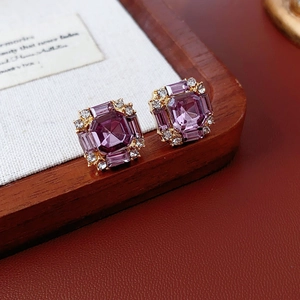 Macro shot of square gold earrings featuring purple octagonal gems and clear zircons
