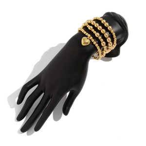 Detail of four-piece gold bead bracelet set featuring a polished heart-shaped pendant charm