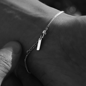 Detailed shot of a silver stainless steel box chain bracelet with an extender and tag